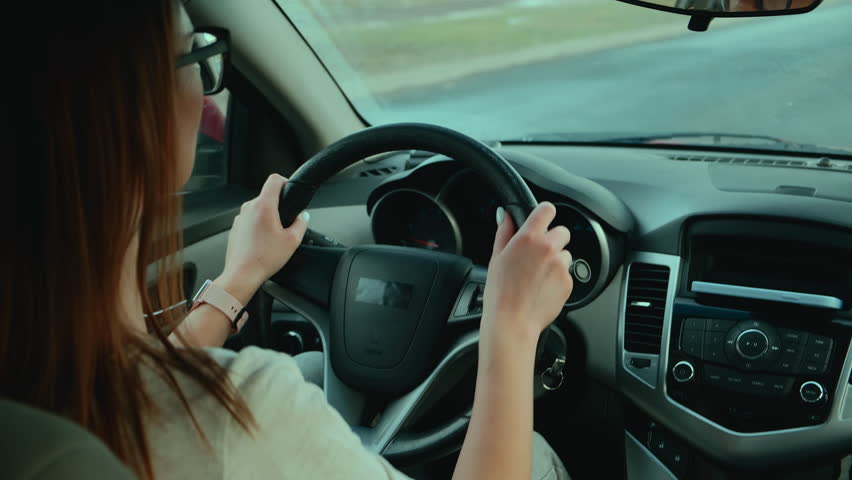 Woman driver control the radio or music on the road while driving a car in motion, Back shot Royalty-Free Stock Footage #1099796539
