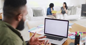 African american man making laptop video call, copy space on screen, colleagues behind, slow motion. Working from home, small business, friendship and start up business concept.
