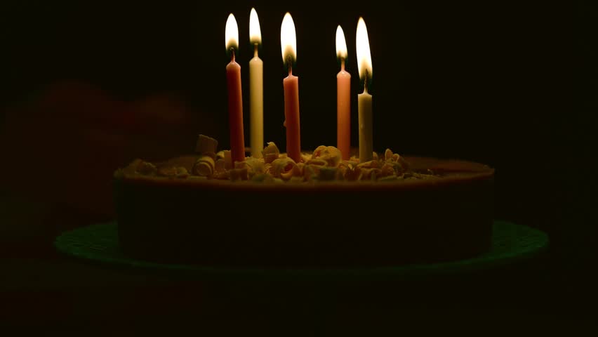 Blowing burning candles on birthday cake, dark background