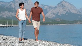 Beautiful middle aged man and woman holding hands while walking on pebble beach - Powered by Shutterstock - Get 15% off with code: PIKWIZARD15