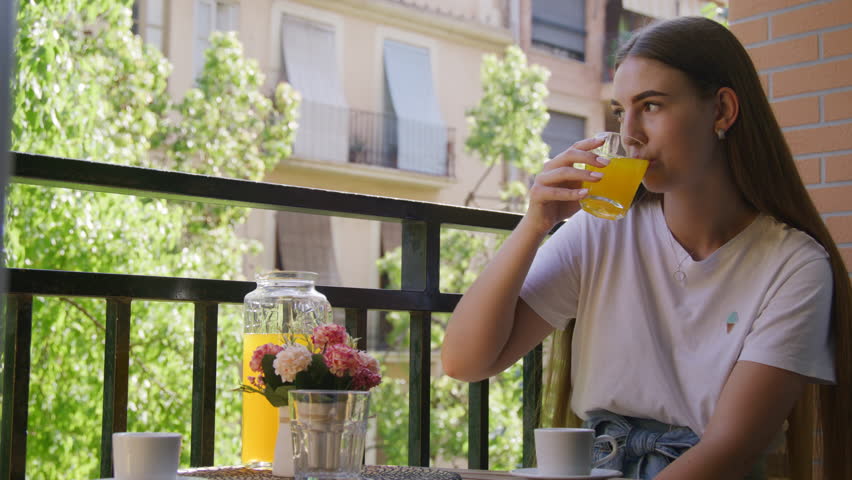 Close-up view of blonde-hairs female teenager enjoying tasty breakfast. Portrait of a thoughtful, young woman drinking fresh orange juice. High quality 4k footage
