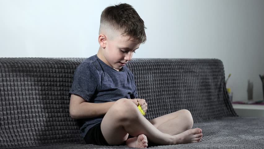 A little boy opening sweets and taking pastila his mouth while sitting on a cozy sofa. A child enjoys candy | Shutterstock HD Video #1099811297