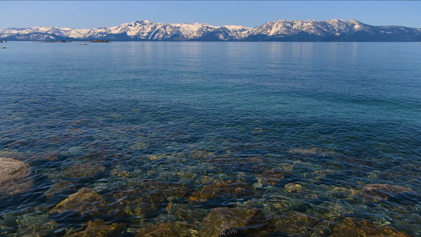 Lake Tahoe - A closeup view of clear blue water of Lake Tahoe, with snow-capped peaks of Sierra Nevada towering at horizon. Lake Tahoe, California, USA.
