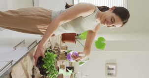 Vertical video of happy caucasian woman watering her plants of basil. Spending quality time at home concept.