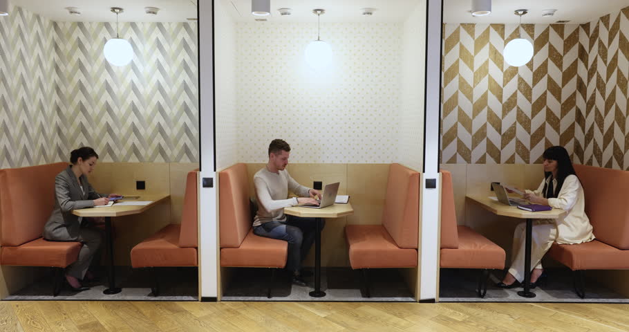 Employees working in separate booths in freelance cafe, co-working space, sitting at divided tables, using paper documents, laptop computers, mobile phones for Internet communication Royalty-Free Stock Footage #1099822923