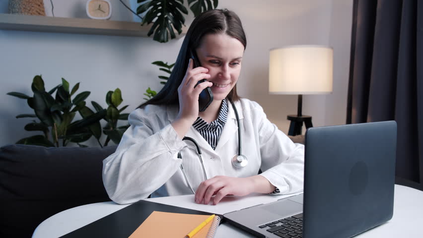 Young woman physician talk by phone before pc. Close up of female doctor consulting sick person by phone fill in files on laptop describe complaints from patient words give advice prescriptions | Shutterstock HD Video #1099824643