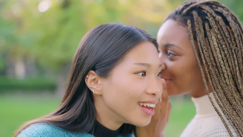 African woman tells friend a secret in her ear outdoors | Shutterstock HD Video #1099825177
