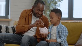 Early financial literacy. Loving african american father teaching his little son to save money, putting coins into piggybank and giving high five to each other, tracking shot, slow motion, free space - Powered by Shutterstock - Get 15% off with code: PIKWIZARD15