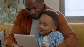 Modern kids development. Close up portrait of cute little african american boy playing education game on digital tablet with his loving daddy, tracking shot, slow motion