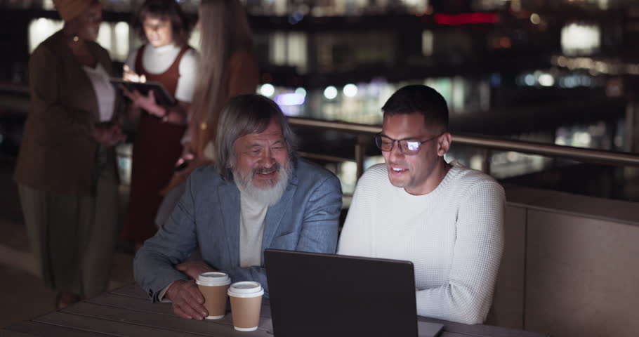 Laptop, collaboration and night with a CEO and employee talking strategy or planning outdoor on the office balcony. Mentor, teamwork and management with a senior man and associate talking outside | Shutterstock HD Video #1099826989