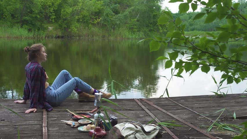 Teen girl having a picnic on a wooden pier at the river bank
 | Shutterstock HD Video #1099830127