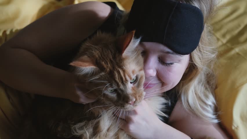 Happy young woman hugging a big ginger Maine Coon cat in bed at home. Pets and people concept