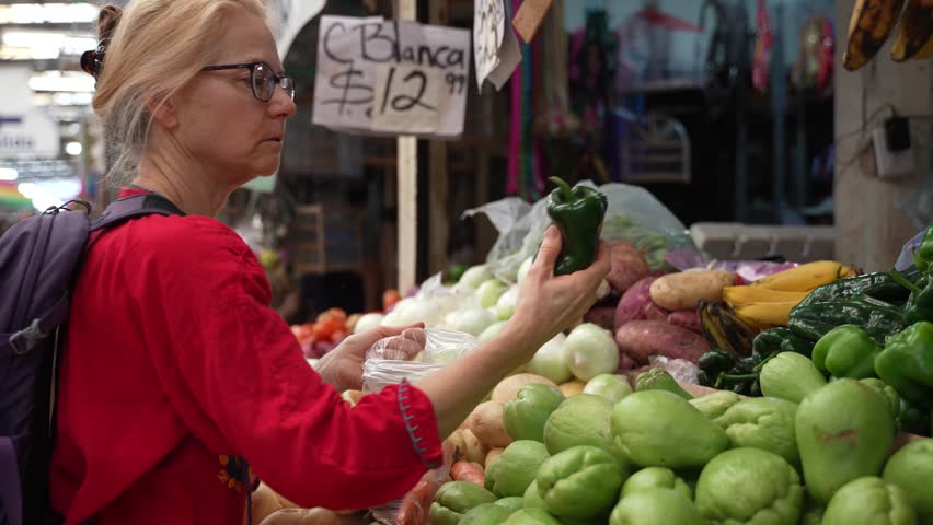 Attractive blonde mature senior woman poblano peppers, vegetables and fruit at a local indoor market in Mexico. | Shutterstock HD Video #1099832661