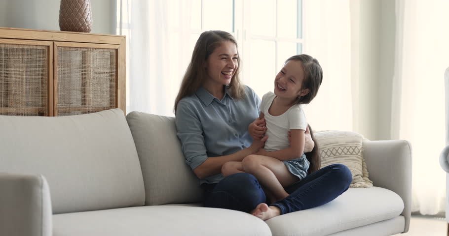 Cute little girl laughing seated on mums laps, enjoy funny playtime and communication with loving mother, relish pastime together on carefree weekend at cozy home. Happy motherhood, custody and love | Shutterstock HD Video #1099835259