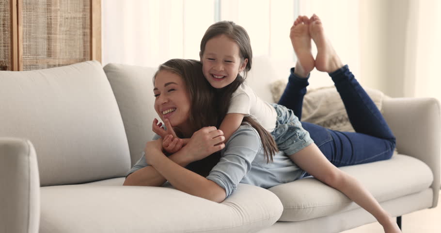 Happy motherhood, family bond, adoption and custody. Young loving mother enjoy warm communication and sweet moments of tenderness, spend time with little adorable daughter lying on cozy sofa at home | Shutterstock HD Video #1099835263