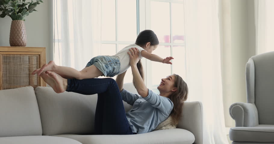 Young mother play with little 5s adorable daughter lifts her on arms, enjoy active playtime together feel happy, having fun on weekend leisure at home. Family games with kids, custody and motherhood Royalty-Free Stock Footage #1099835277