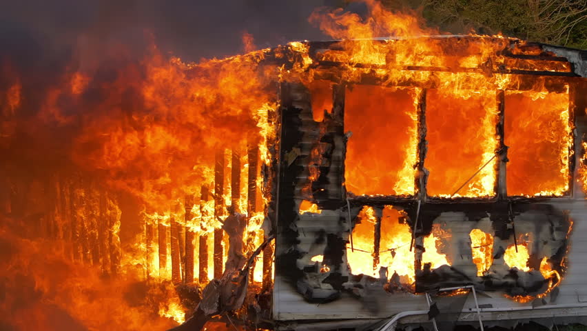 Super slow motion footage of massive flames burning a trailer home. Large house fire ablaze with large flames, falling debris, and smoke. 