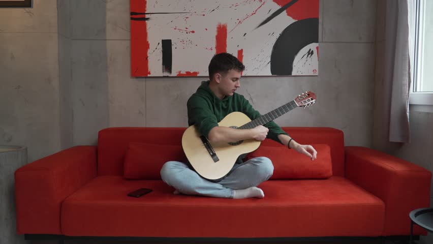 One young man Caucasian teenager sit at home in room playing guitar