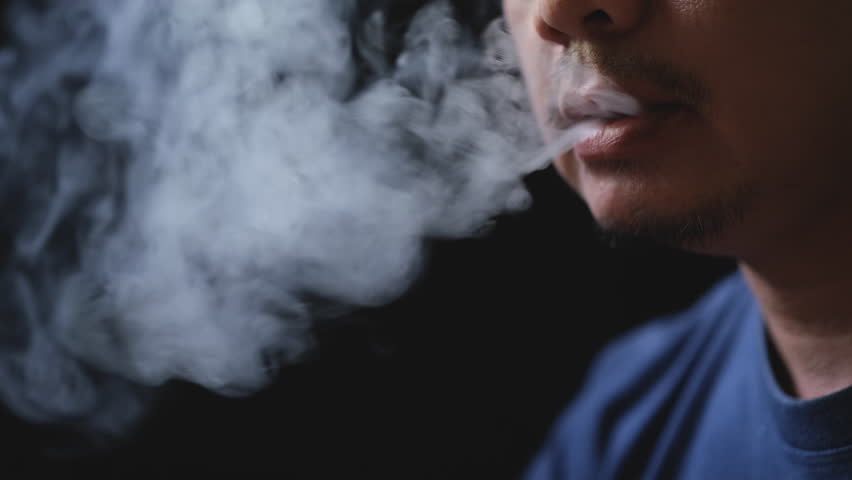 The mouth of an Asian man is smoking an e-cigarette and puffing out white smoke.
 | Shutterstock HD Video #1099844117