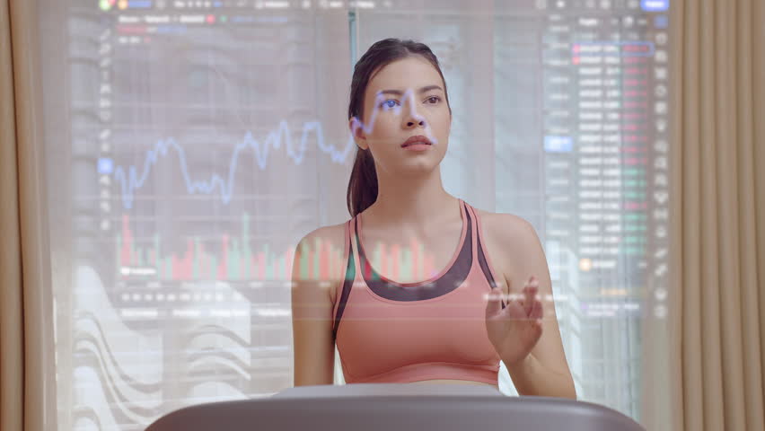 Attractive woman running on a treadmill at home and looking stock market and using hand sliding on the virtual monitor. | Shutterstock HD Video #1099847731