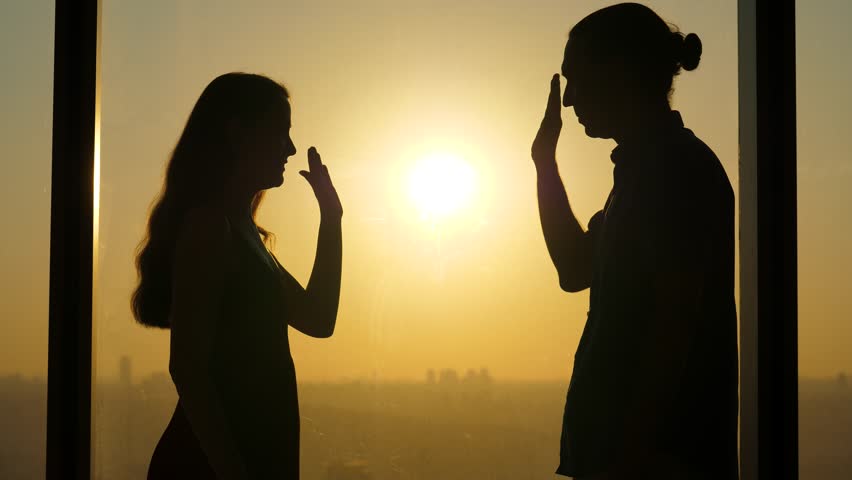 Woman and man raise and slap their hands, silhouetted shot against window, sunny evening. High five gesture from two happy people. Two times slow motion from original clip at 60 fps Royalty-Free Stock Footage #1099847779