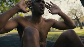 Topless young black man doing sit-ups on pavement surrounded by trees in park