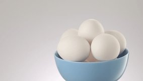 Chicken eggs in a blue bowl moving on a grey background. protein foods. High quality 4k footage