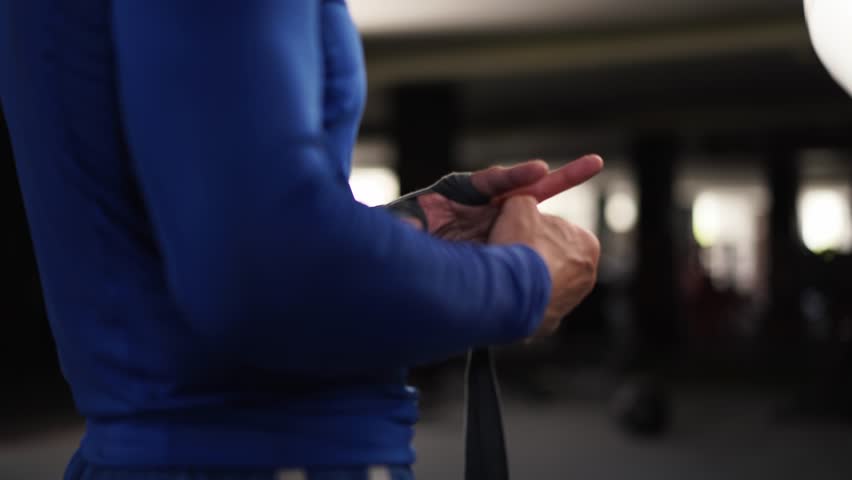 Athletic man wrapping hands with boxing bandages at gym. Male fighter wrapping his hands with black protection bandages. Male athlete preparing for fight in a gym. Sport, active lifestyle concept. 