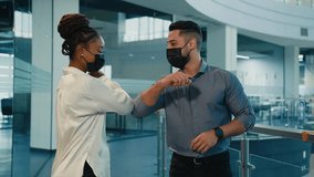 Two diverse colleagues Indian Arabian man businessman and African American woman businesswoman in medical face masks greeting with elbow bump talking friendly together in office hall Coronavirus rules - Powered by Shutterstock - Get 15% off with code: PIKWIZARD15