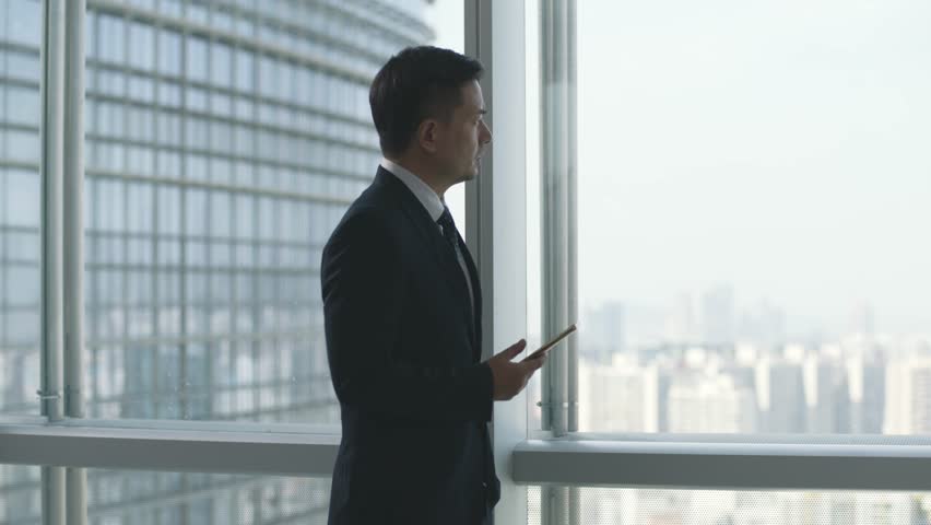 Asian business man looking at cellphone while pacing by the window in office | Shutterstock HD Video #1099854039
