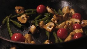 Extreme close-up of vegetables in frying pan. Mushrooms tomatoes asparagus fry in oil. Slow motion - Powered by Shutterstock - Get 15% off with code: PIKWIZARD15
