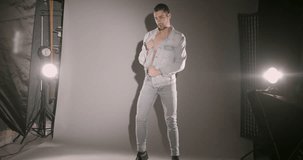 Young male model posing for a photo shoot in jeans isolated on gray, with studio strobe flashing