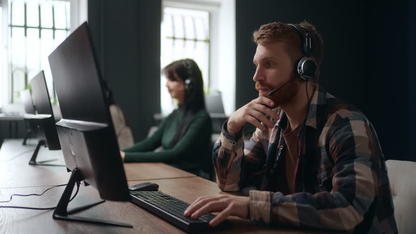 people work in call-center, young bearded man answering on phone call, consulting customers