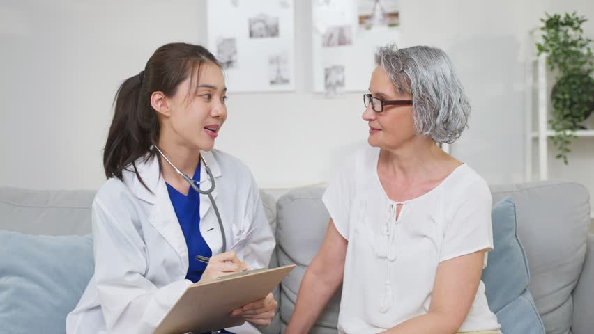 Asian caregiver nurse examine Caucasian senior woman patient at home. Attractive specialist carer women support, give advise and consult with older elderly mature grandmother in living room in house. | Shutterstock HD Video #1099861691