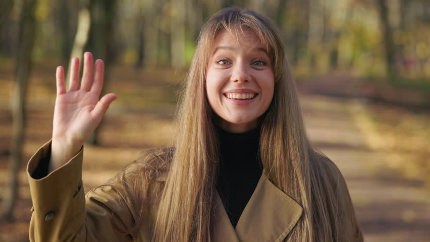 Front view of pretty, cheerful lady walking in park, standing. Glad, happy woman wearing fashionable clothes, looking at camera, waving. Concept of happiness and sincere emotions.