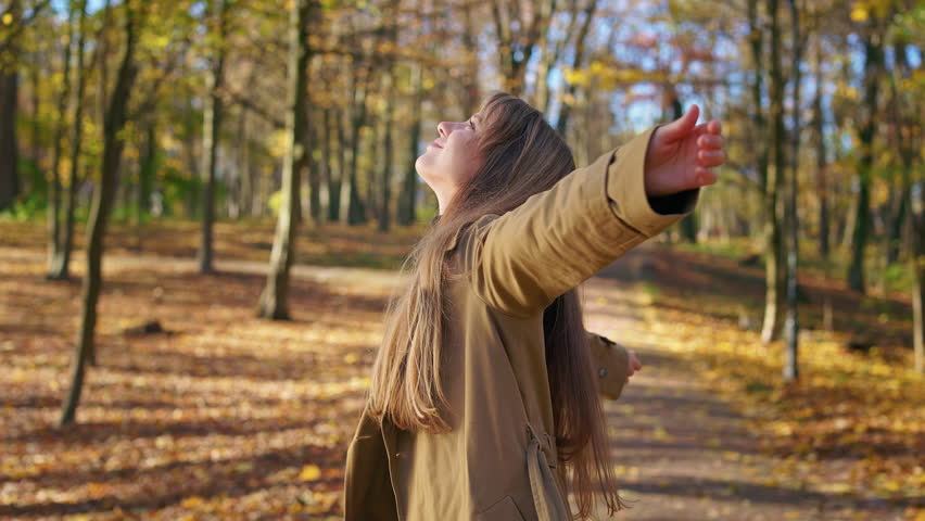 Front view of stylish woman wearing fashionable clothes, enjoying sunny autumn weather. Beautiful lady smiling, stretching hands, admiring, smiling. Concept of beauty of nature. | Shutterstock HD Video #1099864445