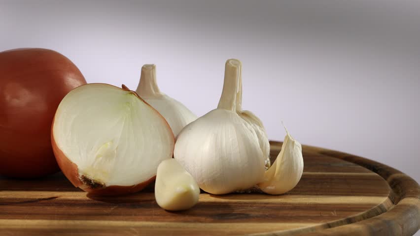 onions and garlic on a cutting board. a clove of garlic and half an onion lie with the whole. vegetables ready for cutting close-up. kitchen on a sunny day. High quality 4k footage