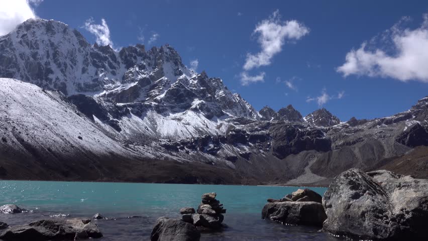 Turquoise bright Gokyo lake with snowy Himalayan mountains 
boulder and cairns in the water, 2023

