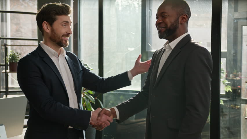 Caucasian boss hr manager man shake hand of African American candidate partner client making deal hiring thanking for collaboration congratulation. Diverse business partners men in office handshaking Royalty-Free Stock Footage #1099872265
