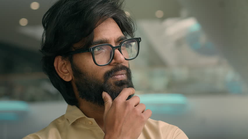 Indian pensive man in eyeglasses thinking. Close up thoughtful male face look distance indoors pondering business idea searching problem solution. Arabian businessman in glasses think touching chin | Shutterstock HD Video #1099874501