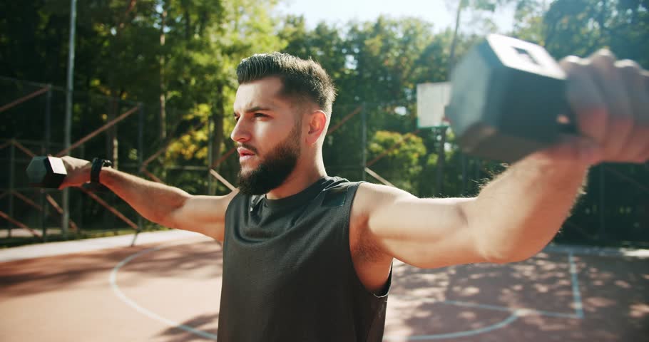 Fit man working out with dumbbells. Gym concept. Healthy lifestyle. dumbbells concentrating working out alone. exercises for the hand muscles. Outdoor training on the field of sports exercises. | Shutterstock HD Video #1099875873