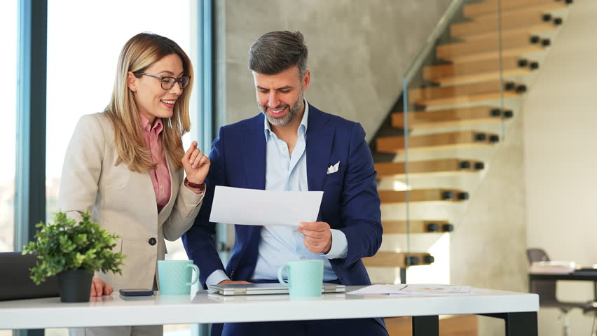 Female and male business managers collaborating on new project at office desk in modern workplace. Senior businessman and female African American colleague intern walking by in background.  | Shutterstock HD Video #1099876483