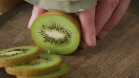 Male hands cutting a fresh kiwi fruit with knife in slices on wooden board. Cooking concept. Close up. 4k video
