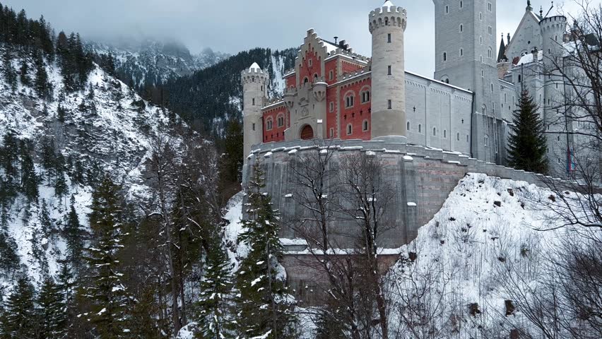 Aerial drone view Neuschwanstein castle on Alps background in vicinity of Munich, Bavaria, Germany, Europe. Winter landscape with castle and lake in snowy mountains covered with spruce forest. 