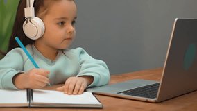 Smart girl with headphones studying online on a laptop, writing in a notebook.