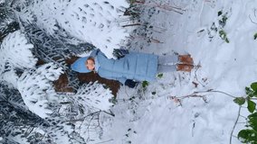 vertical video. snowfall. a cute girl in a blue coat under a snow-covered spruce. the beauty of winter nature, winter games and entertainment with children.