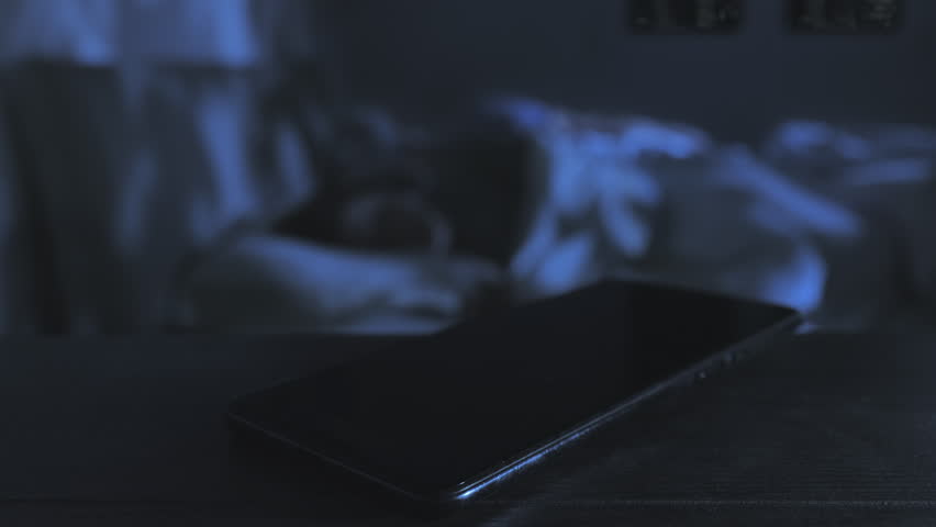 infidelity love affair,close up on mobile phone receiving incoming call while a married couple sleep on bed in the background,betrays cheating concept Royalty-Free Stock Footage #1099881351