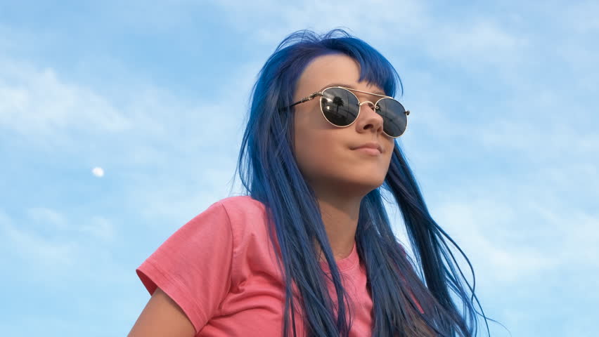 Child with dyed hair color outdoor. A happy smiling child in sunglasses relax and enjoy her dyed blue hairstyle on the shore.