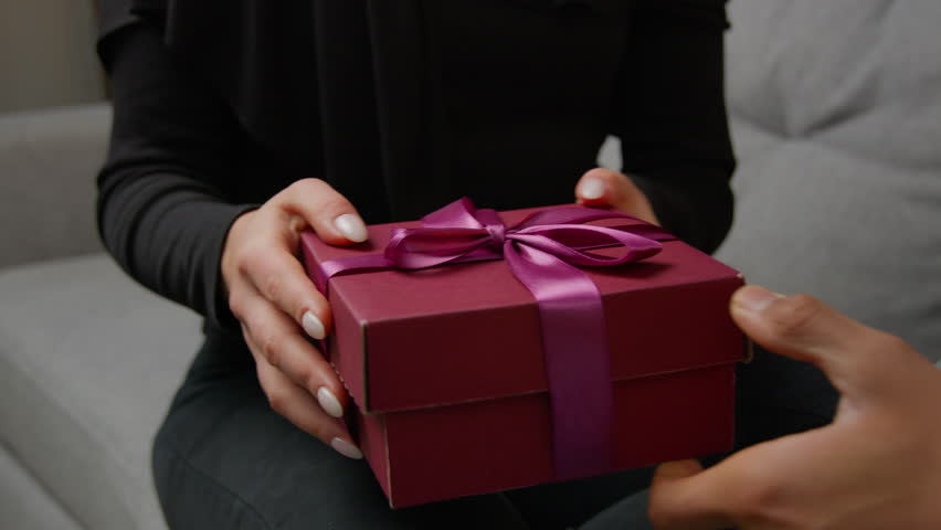 Close up presenting gift on marriage anniversary Valentine love day romantic date unrecognizable female hands unpacking surprise pink box take off ribbon. Cropped view couple man and woman get present Royalty-Free Stock Footage #1099886443