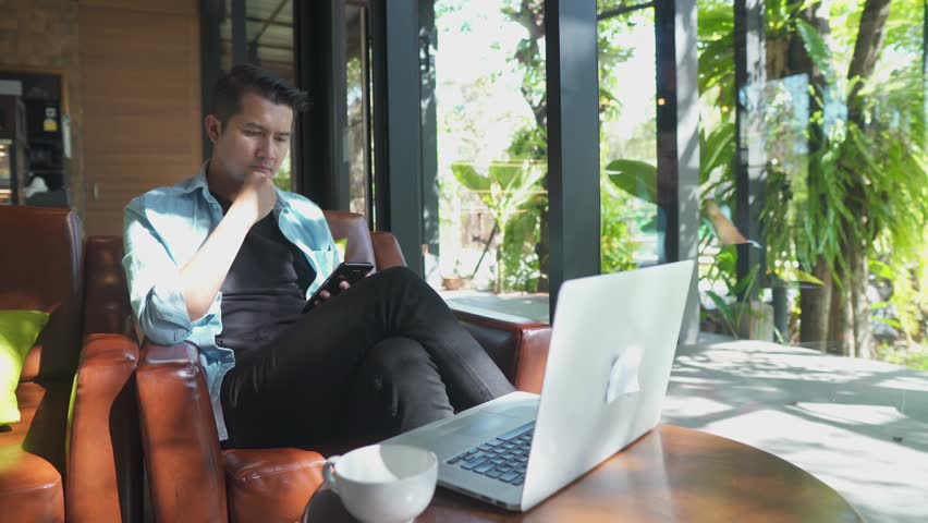 Asia businessman sitting at Cafe with laptop and smartphone.Businessman texting on smart phone while sitting in Cafe. Young people working and checking emails in computer.